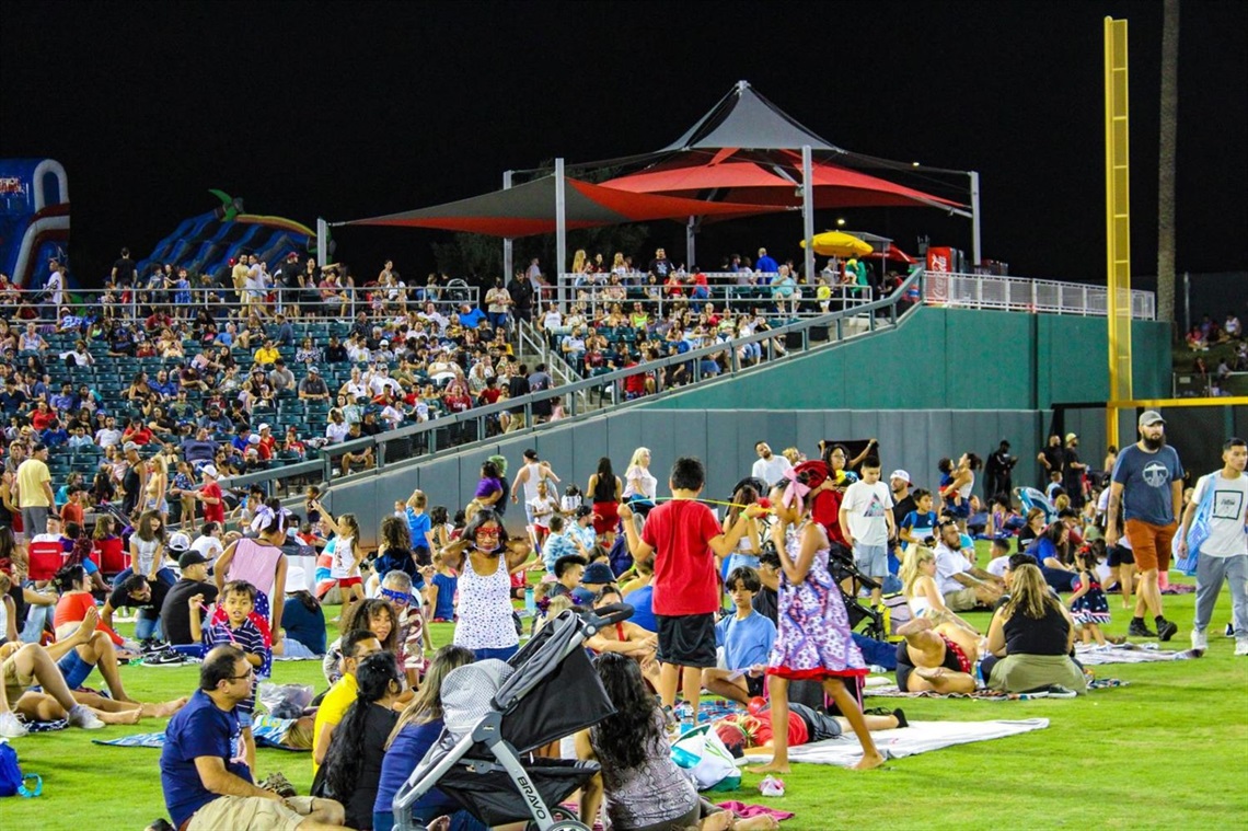 A crowd of people at an event. Some are in the seats, and some are on the grass.